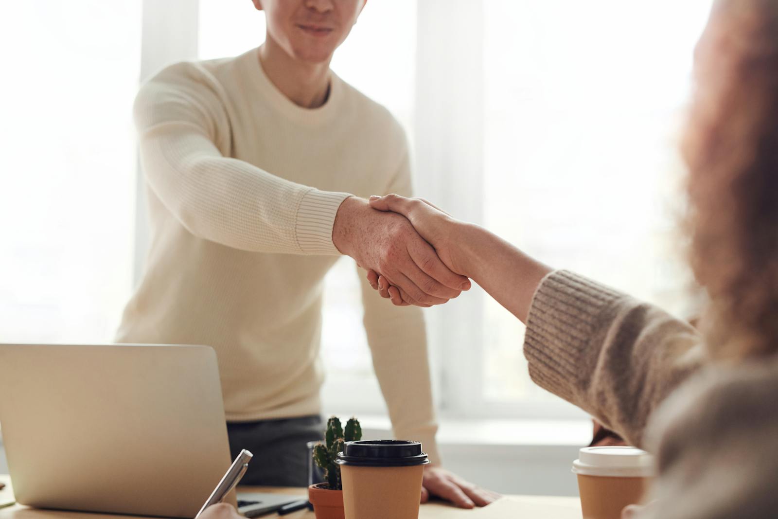 Gros plan de professionnels se serrant la main autour d'un café dans un bureau moderne.