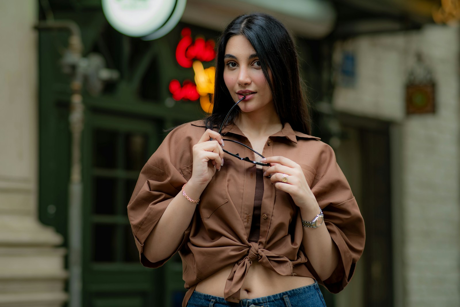 Young woman holding sunglasses in front of storefront.